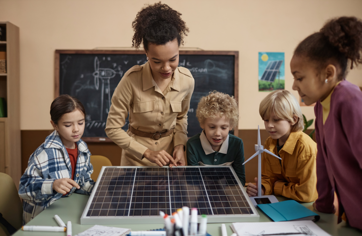 A teacher with 3 children looking at scale models of solar panels and wind generators